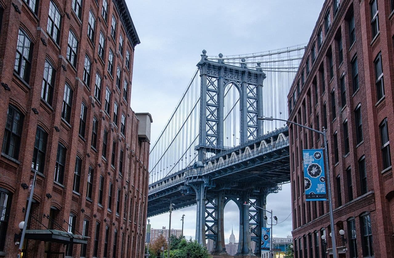 The manhattan bridge is in the center framed by two old brick buildings. It is a cloudy afternoon.
